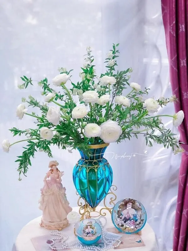Hoa cắm tết có một chiếc bình màu xanh với những bông trắng trong đó trên bàn
