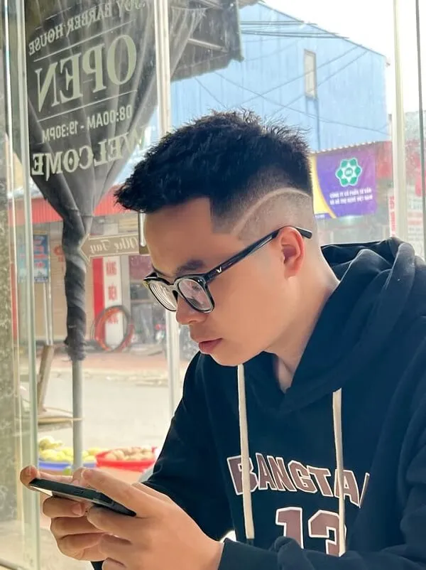 Kiểu tóc mohican dài có một người đàn ông ngồi bàn nhìn vào điện thoại di động của anh ấy