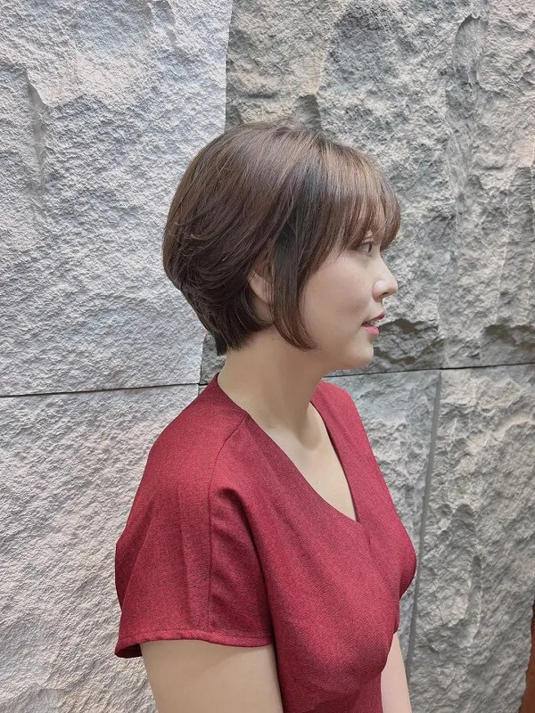 Tóc tém tomboy người phụ nữ châu mặc áo đỏ đứng trước bức tường đá với điện thoại di động trong tay