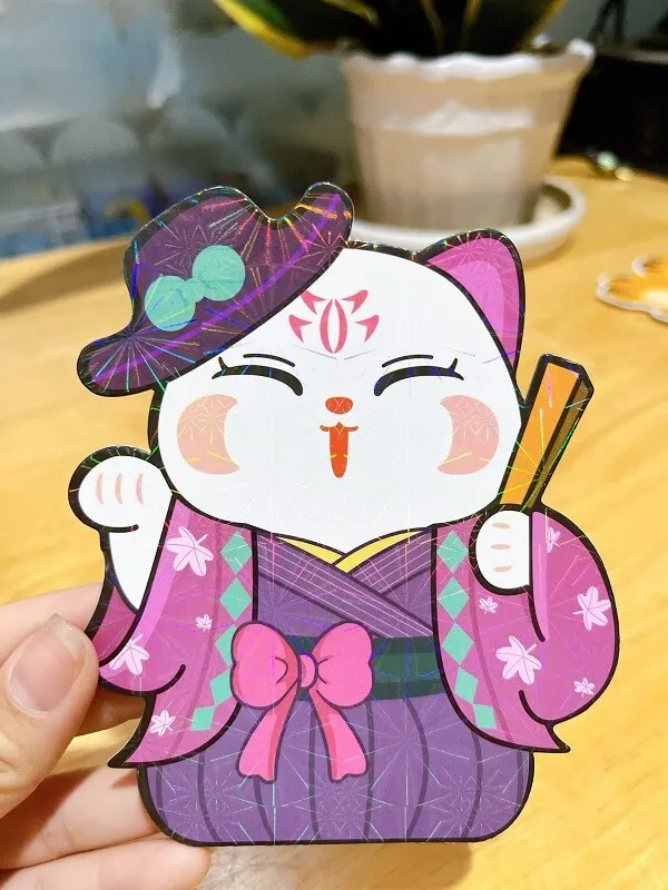Ảnh lì xì ai đó đang cầm một cái giấy cutout của con mèo mặc kimono màu tím