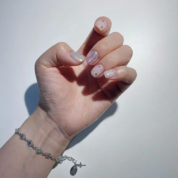 Mẫu nail đơn giản sang trọng bàn tay của người phụ nữ với móng màu hồng và trắng cầm dây xích bạc