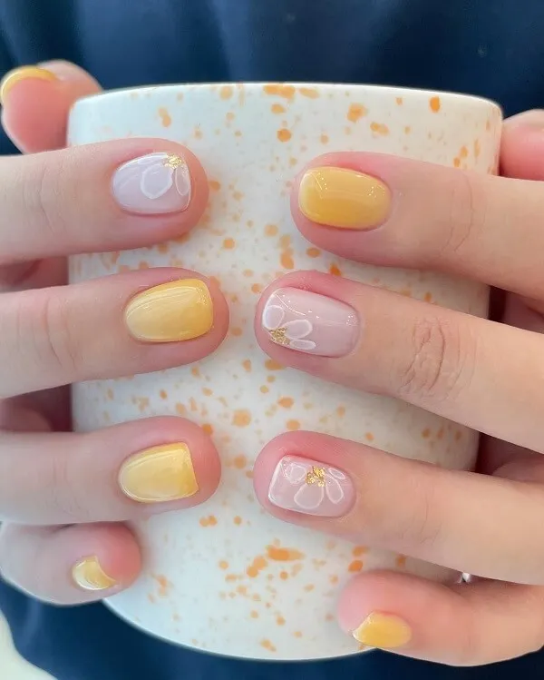 Mẫu nail đơn giản có một người cầm cốc với thiết kế màu vàng và trắng trên đó