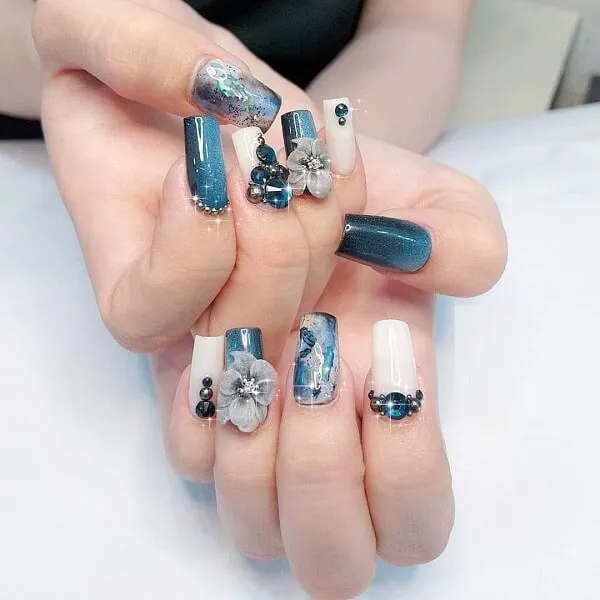 Mẫu nail tết có một người phụ nữ cầm móng tay màu xanh và trắng với hoa trên đó
