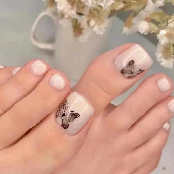 Nail chân màu trắng sữa ai đó đang lấy ngón của họ được vẽ bằng một thiết kế bướm trên chúng