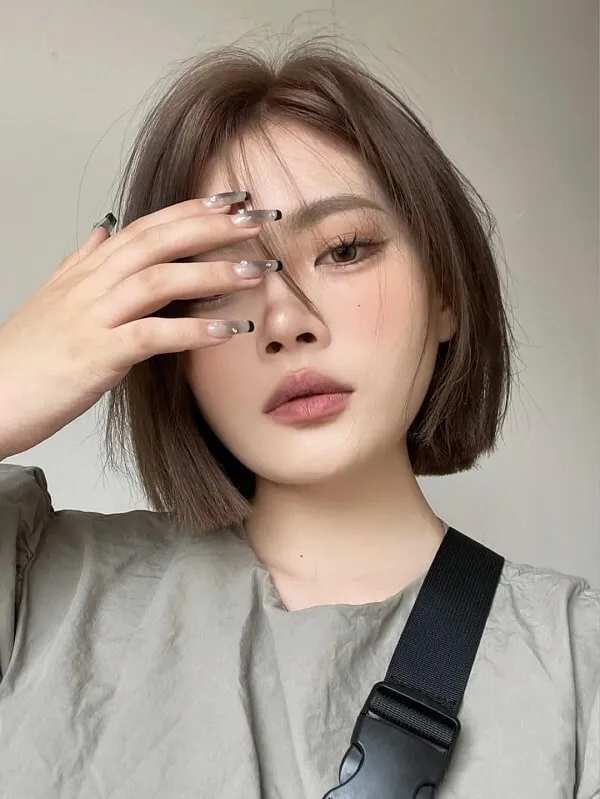 Mẫu tóc bob ngắn người phụ nữ châu với mái màu nâu mặc áo xám và túi đeo vai đen