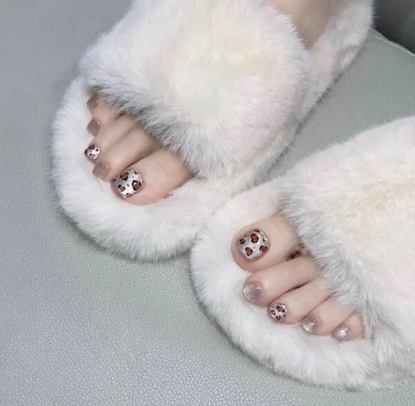 Mẫu nail chân đẹp đôi của người phụ nữ trong dép lông xù với các chấm polka trên chúng