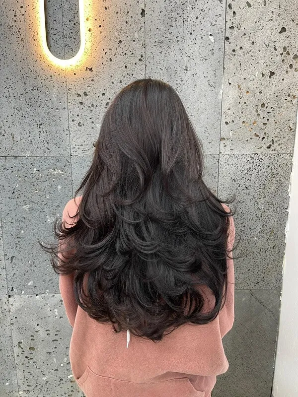 Những kiểu tóc xoăn dài đẹp có một người phụ nữ mái đen đứng trước tường
