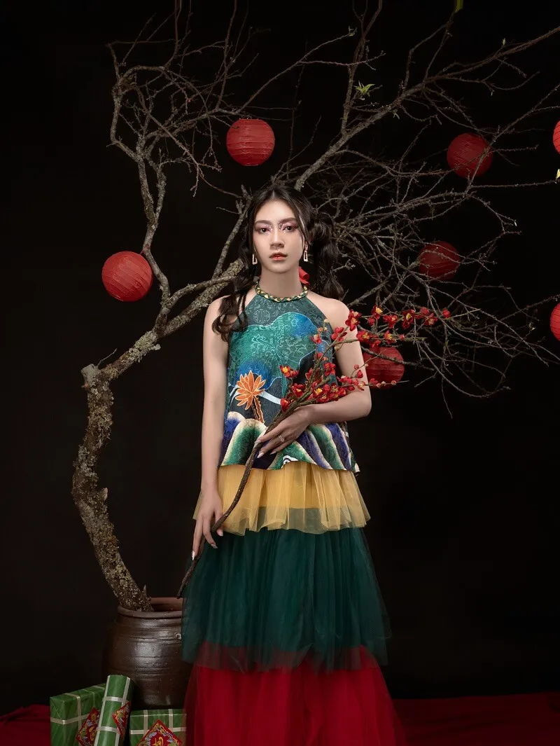 Chụp ảnh tết chân dung của một người phụ nữ trong chiếc váy nhiều màu đứng trước cây với đèn lồng đỏ và xanh lá