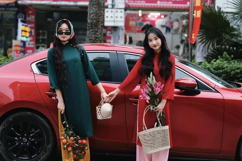 Chụp ảnh tết có hai người phụ nữ đang đứng cạnh một chiếc xe màu đỏ