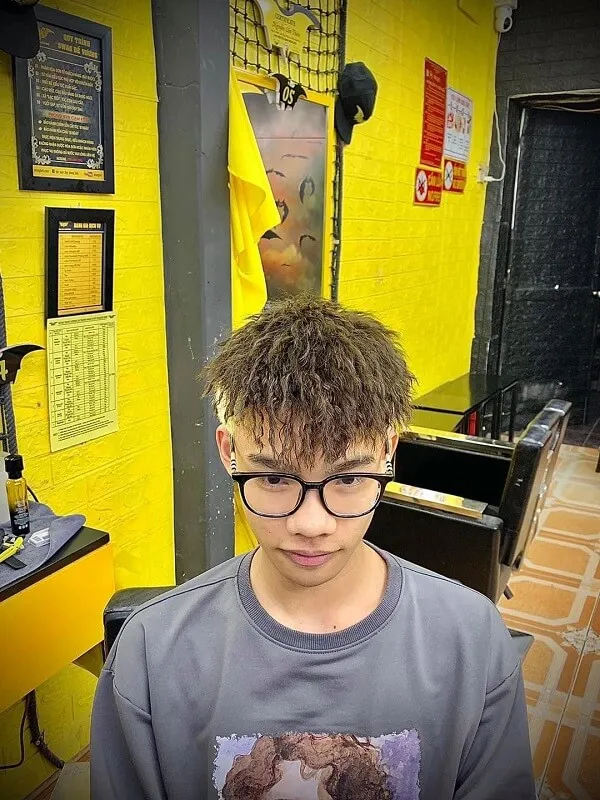 Tóc mohican ngắn có một chàng trai trẻ với kính đứng trước bức tường màu vàng