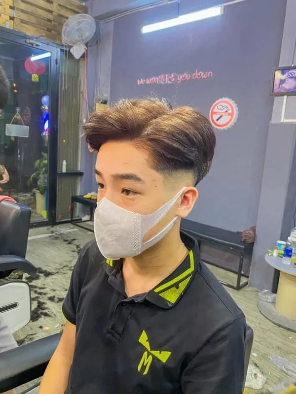Tóc nam side part có một người đàn ông ngồi trên ghế cắt đeo mặt nạ