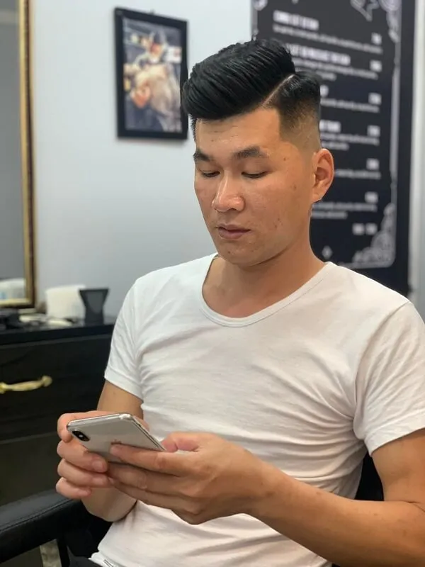 Tóc nam undercut có một người đàn ông ngồi trên ghế nhìn vào điện thoại di động của anh ấy