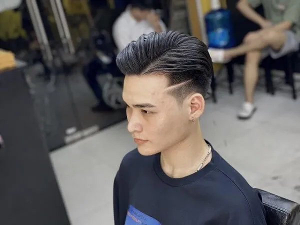 Tóc side part nam có một người đàn ông ngồi trên ghế với chiếc áo sơ mi đen