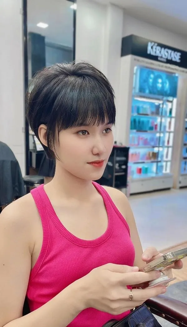Tóc tomboy người phụ nữ châu trong chiếc áo tăng màu hồng nhìn vào điện thoại di động của cô ấy