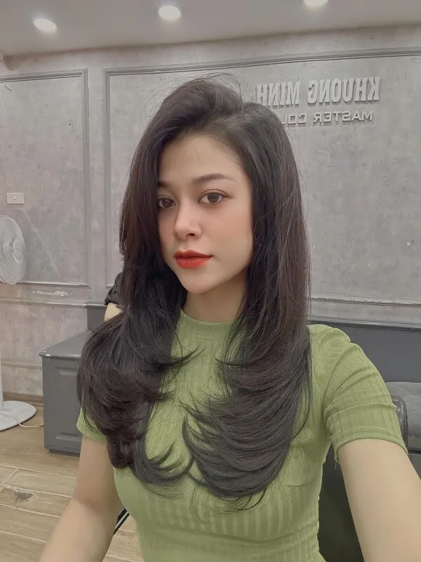 Tóc uốn chữ người phụ nữ có mái đen dài mặc váy màu xanh lá cây và son môi đỏ