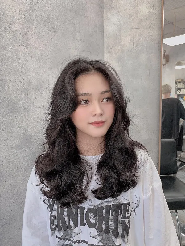 Tóc dài uốn xoăn sóng nước chân dung một người phụ nữ có mái đen đứng trước bức tường màu xám