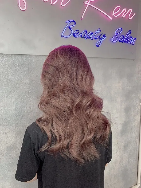Tóc xoăn sóng lơi ngang lưng người phụ nữ vàng với mái dài gợn đứng trước một dấu hiệu thẩm mỹ viện