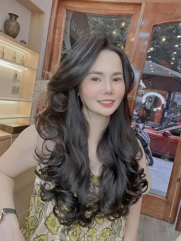 Tóc xoăn sóng lơi ngang lưng có một người phụ nữ mái đen dài đứng trước cửa sổ